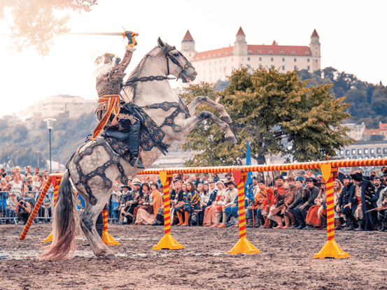 Rytier s mečom v ruke na koni na zadných nohách. Dobovú ukážku na Tyršovom nábreží sledujú diváci, v pozadí na druhom brehu Dunaja sa vyníma Bratislavský hrad.
